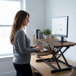 Woman standing at a black standing desk converter with dual monitors in a modern office