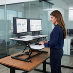 Woman standing at a black standing desk converter with dual monitors in a modern office
