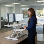 Woman standing at a black standing desk converter with dual monitors in a modern office