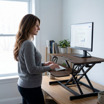 Woman standing at a black standing desk converter with dual monitors in a modern office
