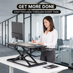 Woman taking notes at a raised standing desk converter in an open office