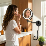Woman applying makeup using a wall-mounted LED magnifying mirror at a bathroom vanity