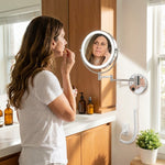 Woman applying makeup using a wall-mounted LED magnifying mirror at a bathroom vanity