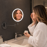 Woman adjusting a wall mounted LED magnifying makeup mirror in a bathroom vanity setting