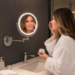 Woman adjusting a wall mounted LED magnifying makeup mirror in a bathroom vanity setting