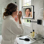 Woman using the wall-mounted makeup mirror at a bathroom vanity