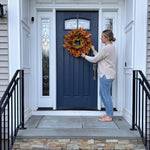 Woman hanging an artificial fall wreath on a front door