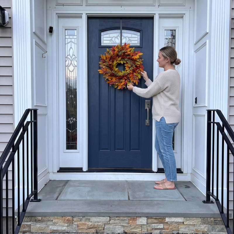 Woman hanging an artificial fall wreath on a front door